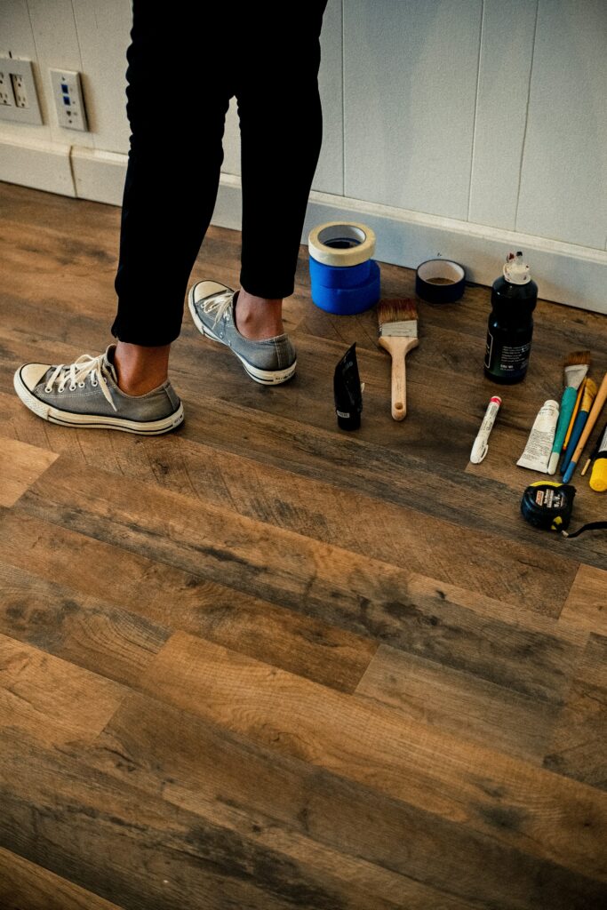 Person standing on wooden floor surrounded by DIY equipment such as paint brushes and masking tape